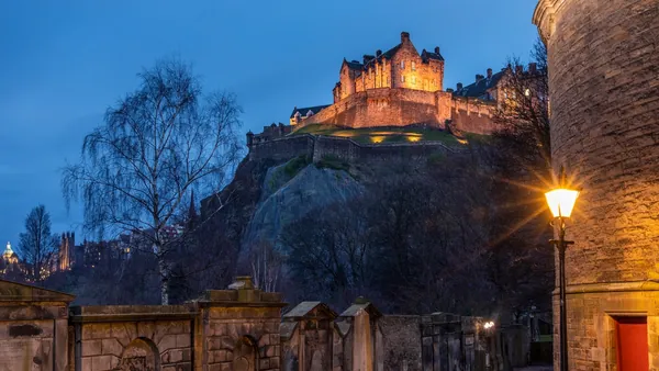 Castillo de Edimburgo iluminado por la noche visto desde el Old Town con lápidas en primer plano