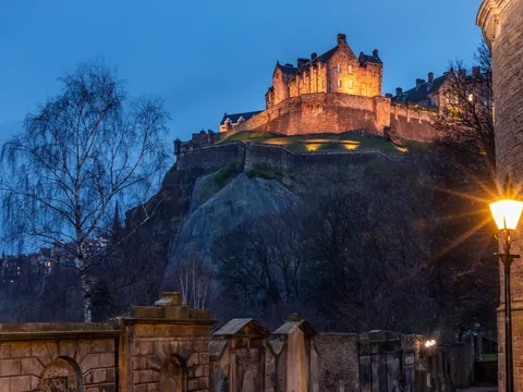 Castillo de Edimburgo iluminado por la noche visto desde el Old Town con lápidas en primer plano