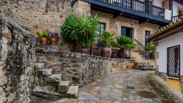 Calle empedrada con casas tradicionales y plantas en macetas en Lastres, Asturias.