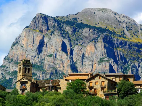 Casas de piedra con torre de iglesia bajo la Peña Montañesa en Aínsa, Huesca.