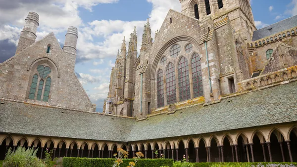 Claustro y fachada gótica de la abadía del Mont Saint-Michel en Normandía, Francia, con arcos y ventanales históricos.