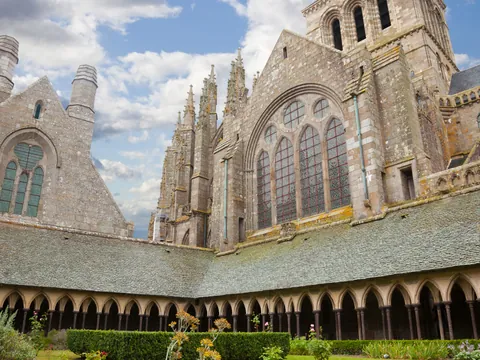 Claustro y fachada gótica de la abadía del Mont Saint-Michel en Normandía, Francia, con arcos y ventanales históricos.