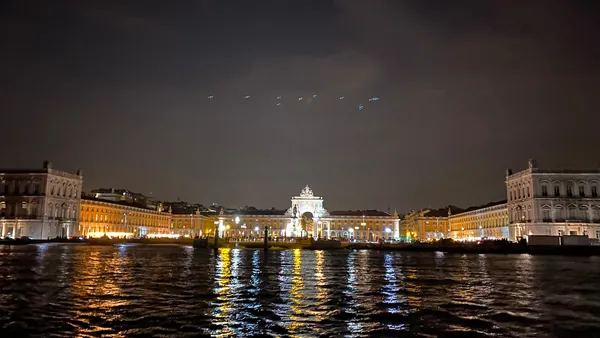 Vista nocturna de la Plaza del Comercio en Lisboa iluminada, con reflejos de luces en el río Tajo y cielo oscuro.