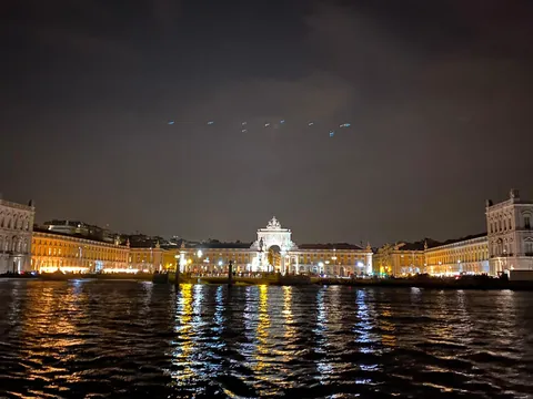 Vista nocturna de la Plaza del Comercio en Lisboa iluminada, con reflejos de luces en el río Tajo y cielo oscuro.