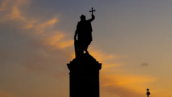 Silueta de la estatua de Pelayo alzando la Cruz de la Victoria al atardecer en Gijón.