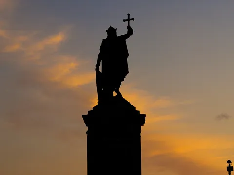 Silueta de la estatua de Pelayo alzando la Cruz de la Victoria al atardecer en Gijón.