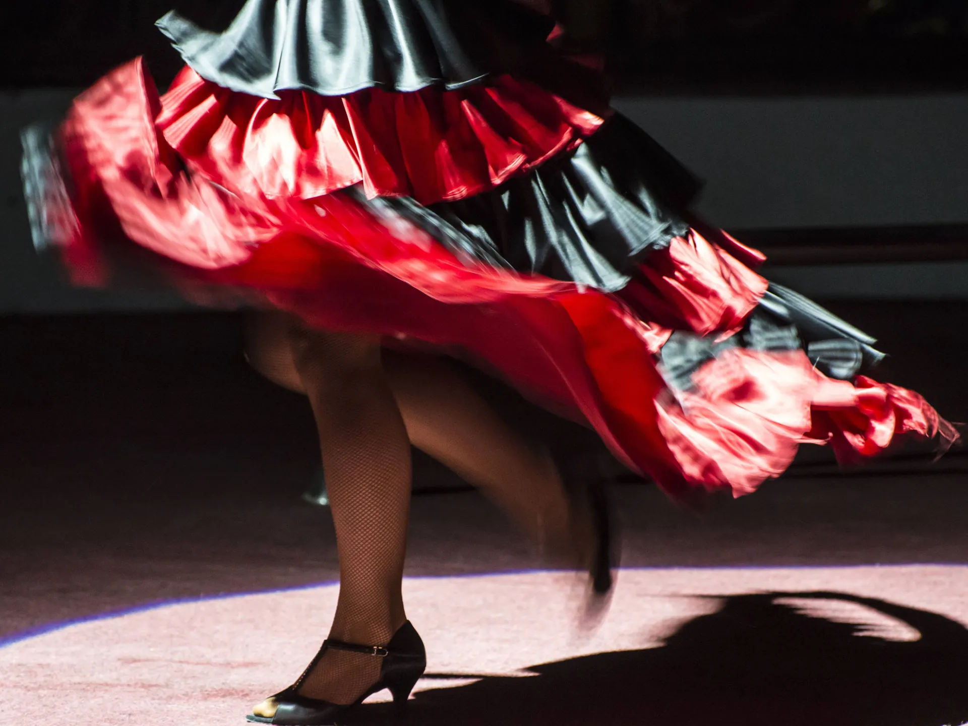 Mitad inferior de una mujer bailando flamenco sobre un tablao flamenco vestida de sevillana, España