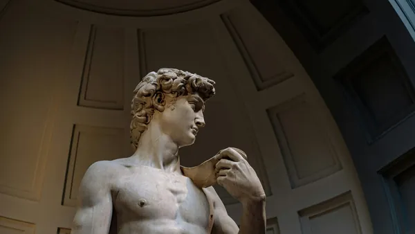 Escultura del David de Miguel Ángel en la Galería de la Academia de Florencia, mostrando detalles del torso y la mano que sostiene la piedra, con fondo arquitectónico clásico.