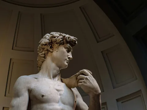 Escultura del David de Miguel Ángel en la Galería de la Academia de Florencia, mostrando detalles del torso y la mano que sostiene la piedra, con fondo arquitectónico clásico.