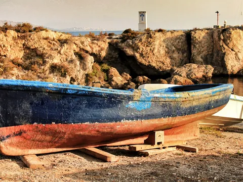 Barca de pesca tradicional azul y roja varada en la orilla de Tabarca con acantilados y el mar de fondo.
