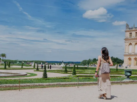 Una mujer con un vestido blanco camina hacia el Palacio de Versalles, mostrando su majestuosa fachada exterior.