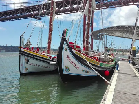 Moliceiros tradicionales junto al Puente 25 de Abril en un día soleado.
