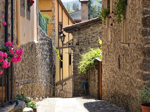 Callejón empedrado con casas de piedra y flores rosas en Potes, Cantabria