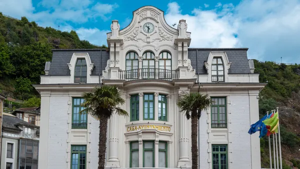 Fachada modernista de la Casa Ayuntamiento de Luarca, Asturias, con palmeras y reloj central.