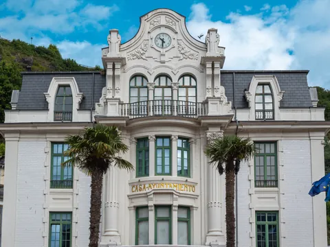 Fachada modernista de la Casa Ayuntamiento de Luarca, Asturias, con palmeras y reloj central.