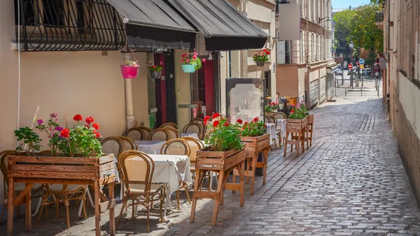 Calle empedrada en Montmartre, París, con mesas y sillas de madera decoradas con flores frente a un café, bajo luz natural en un entorno bohemio.