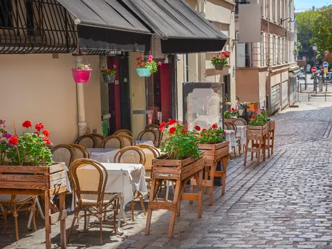 Calle empedrada en Montmartre, París, con mesas y sillas de madera decoradas con flores frente a un café, bajo luz natural en un entorno bohemio.