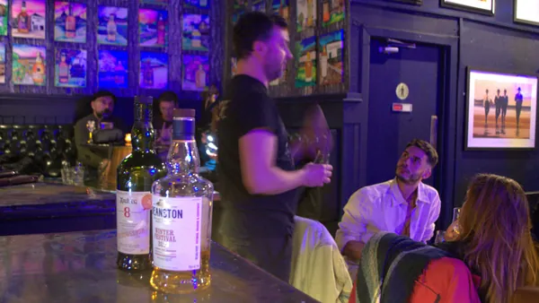 Sesión de cata de whisky escocés en un bar, con dos botellas de whisky en primer plano y personas participando en la actividad.