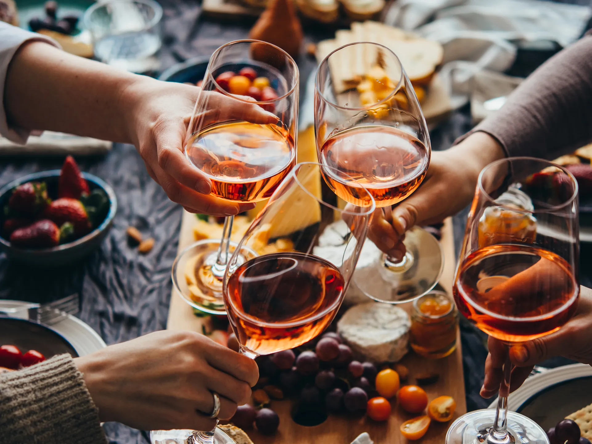 Vasos con vino rosado brindando sobre una mesa con comida