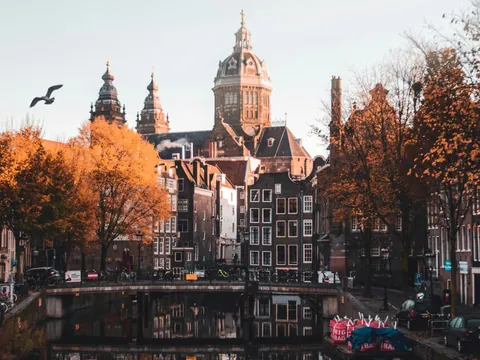 Canal de Ámsterdam con edificios reflejados en el agua y árboles otoñales