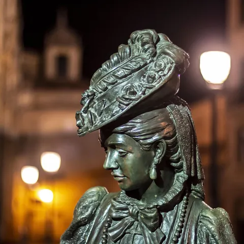 Estatua de bronce de 'La Regenta' (Ana Ozores) en Oviedo, iluminada por farolas urbanas en la oscuridad de la noche.