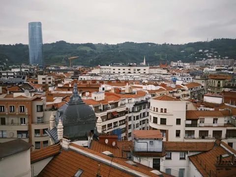 Tejados del centro de Bilbao con la torre Iberdrola y montes verdes al fondo.