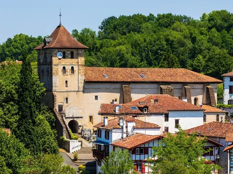 Iglesia de San Esteban rodeada de casas tradicionales blancas y bosque en el pueblo navarro de Bera.