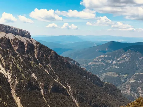 Vistas panorámicas del Valle de Canfranc, Pirineo Aragonés, con laderas boscosas y picos bajo un cielo azul con nubes.