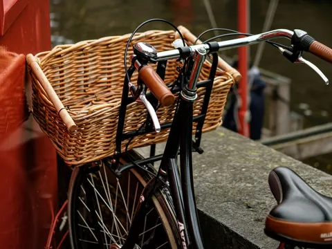 Bicicleta negra con cesta de mimbre apoyada junto a un canal en el centro de Brujas, Bélgica