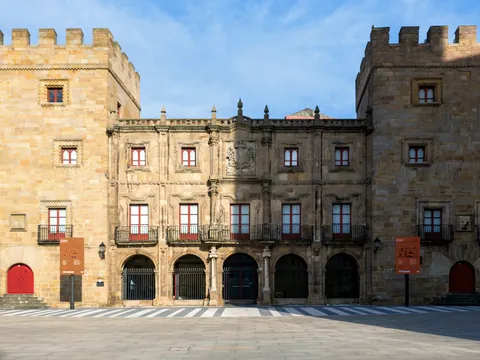 Fachada del histórico Palacio de Revillagigedo en Gijón, construido en piedra con torres y balcones frente a una plaza