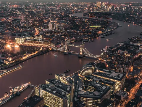 Vista aérea nocturna de Londres con el Tower Bridge iluminado cruzando el Támesis y la Torre de Londres en primer plano.