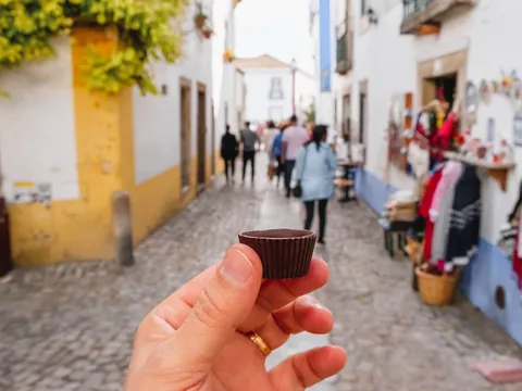 Mano sosteniendo una ginjinha en vaso de chocolate en una calle de Óbidos