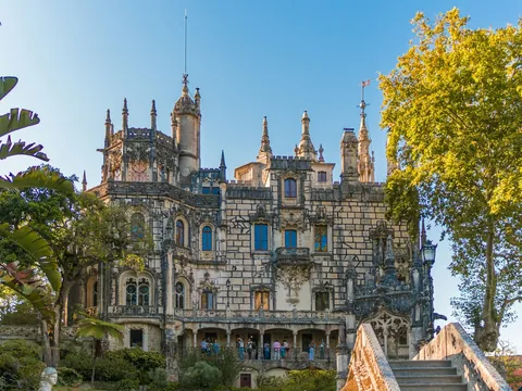 Fachada del palacio de la Quinta da Regaleira rodeada de árboles en un día soleado.