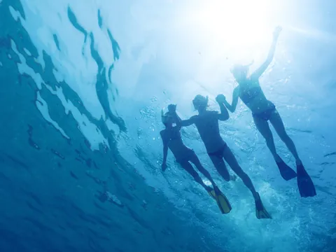 Siluetas de tres personas buceando bajo el mar en Menorca