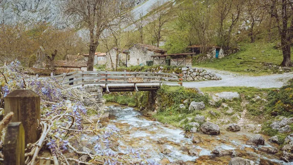 Puente de madera sobre el río Bulnes, en los Picos de Europa, rodeado de casas de piedra y un paisaje natural típico asturiano.