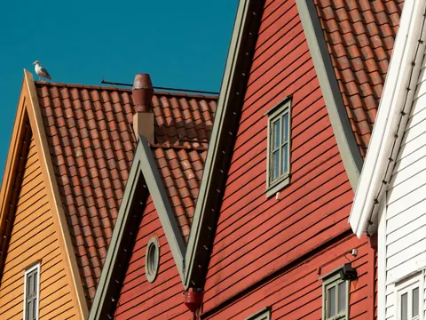 Fachadas rojas y amarillas de las casas de madera de Bryggen, Bergen, Noruega, con tejas y gaviota en el tejado.