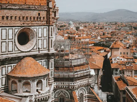 Vista detallada de la Catedral de Santa María del Fiore en Florencia, Italia, mostrando la fachada con mármol policromado y tejados de terracota, junto al paisaje urbano y montañas al fondo.
