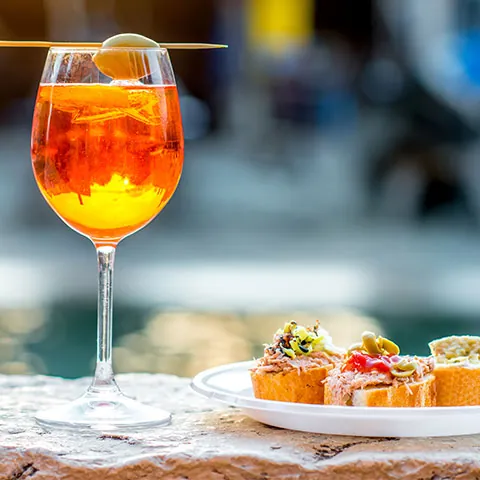 Spritz Aperol bebe con aperitivos venecianos tradicionales cicchetti en el fondo del canal de agua en Venecia.