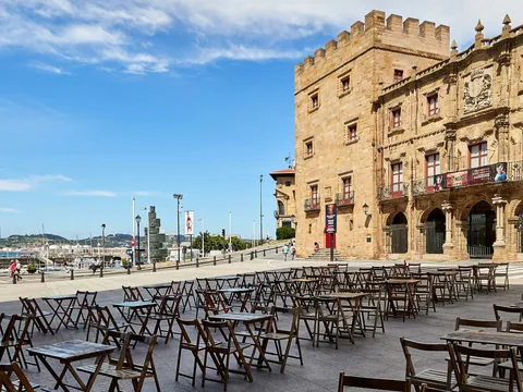 Terraza con mesas frente al Palacio de Revillagigedo y vistas al puerto deportivo de Gijón en un día soleado