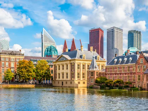 Vista panorámica del Hofvijver en La Haya, Países Bajos, con edificios históricos rodeando el estanque en primer plano y modernos rascacielos de cristal y metal al fondo