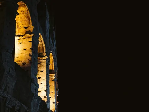 Arcos iluminados del Coliseo Romano resaltando sobre un fondo negro nocturno.