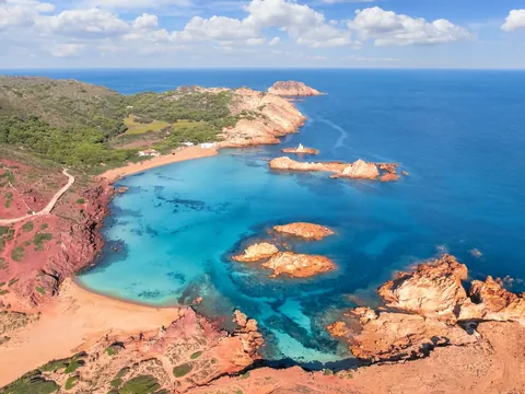 Vista aérea de Cala Pregonda con sus aguas turquesas y rocas rojas en Menorca