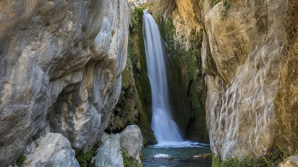 Gran cascada de las Fuentes del Algar cayendo con efecto seda entre altos acantilados rocosos y vegetación.