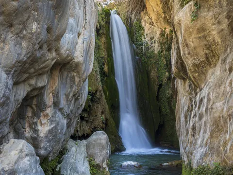 Gran cascada de las Fuentes del Algar cayendo con efecto seda entre altos acantilados rocosos y vegetación.