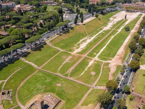 Vista aérea del Circo Máximo en Roma, antiguo hipódromo romano rodeado de árboles y calles, con áreas verdes y restos arqueológicos.