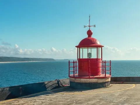 Faro rojo en el fuerte de Nazaré con vistas al océano Atlántico y costa de fondo.