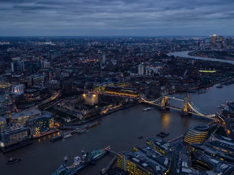 Vista aérea panorámica del río Támesis en Londres con el Puente de la Torre iluminado y la Torre de Londres al anochecer.