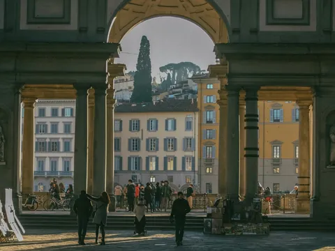 Vista desde el patio de la Galería Uffizi en Florencia, Italia, mostrando arcos monumentales, esculturas clásicas y edificios históricos iluminados por la luz del atardecer.
