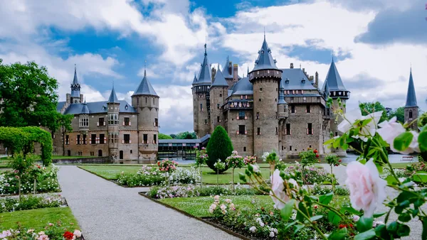 Jardines floridos con rosas frente al Castillo de Haar en los Países Bajos, con el majestuoso edificio medieval de torres y muros de ladrillo en el fondo. y un cielo parcialmente nublado