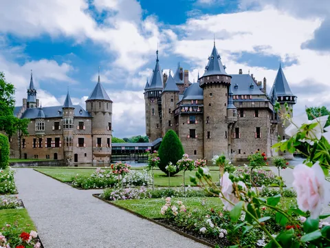 Jardines floridos con rosas frente al Castillo de Haar en los Países Bajos, con el majestuoso edificio medieval de torres y muros de ladrillo en el fondo. y un cielo parcialmente nublado